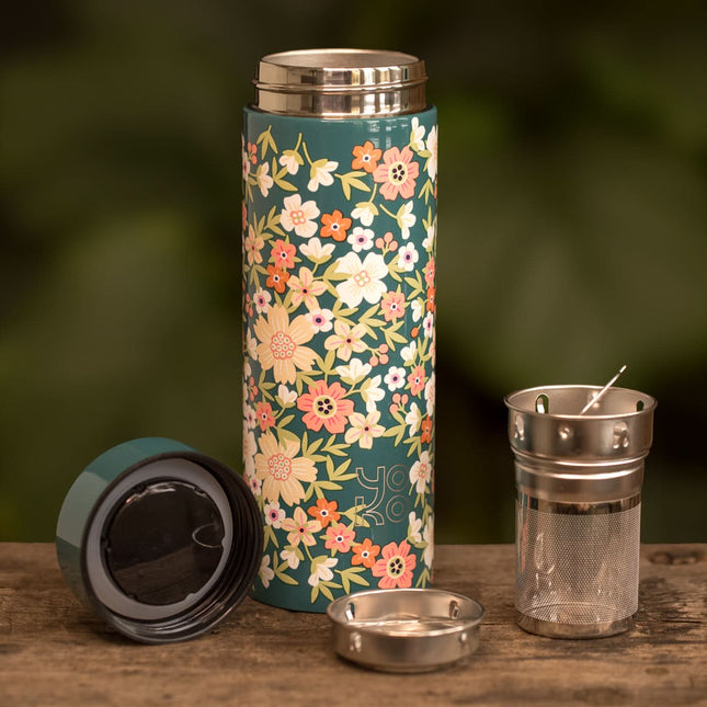 Een geïsoleerde drinkfles van 350 ml met bloemenprint, metalen theezeef en twee doppen staat op hout met groene achtergrond.