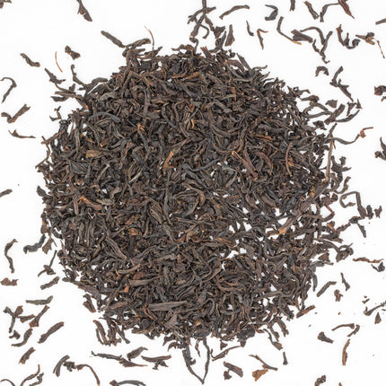 Losse biologische Ceylon BOP1 Lumbini thee van De Theeplantage op een witte ondergrond, met wat theeblaadjes ernaast.