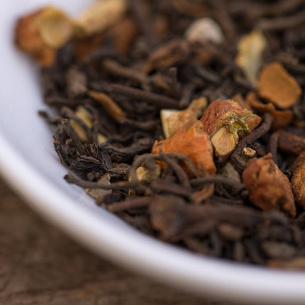 Close-up van Nutcracker Noire biologische losse thee in een witte kom, met stukjes noten en kruiden duidelijk zichtbaar.