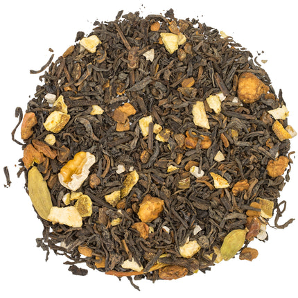 Close-up van de biologische chai melange Nutcracker Noire met losse zwarte thee, noten, stukjes gember, kaneel en kardemom op wit.