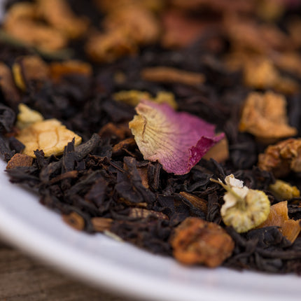 Close-up van Santas Brew biologische kerstthee met losse thee, gedroogde bloemen en fruitstukjes op een wit bord.