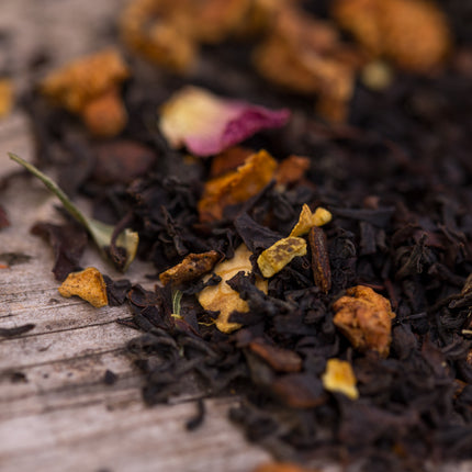 Santas Brew biologische losse Assam thee met stukjes gedroogd fruit en bloemblad op een houten ondergrond.