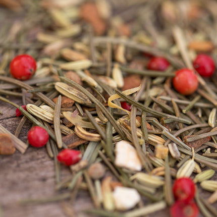 Close-up van Spar & Sparkle biologische losse thee van De Theeplantage met rozemarijnnaalden, venkelzaad, roze peper en stukjes op hout.