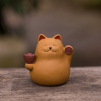 Kleine bruine keramieken kat met opgeheven poot en kopje in de hand, vaak gebruikt als theemascotte bij losse thee.