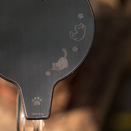 Close-up van een donkere, glanzende theepot met gegraveerde katten, pootafdrukken en onderaan het logo „01Living“.