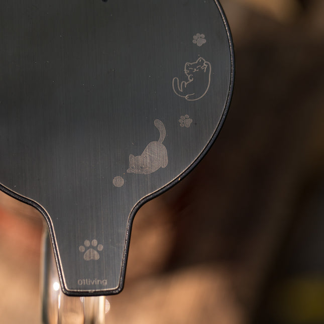 Close-up van een donkere, glanzende theepot met gegraveerde katten, pootafdrukken en onderaan het logo „01Living“.