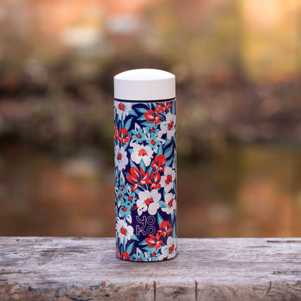 RVS drinkfles van 350 ml met witte dop en rood-wit-blauw bloemenpatroon staat op verweerd hout in een natuurlijke omgeving.