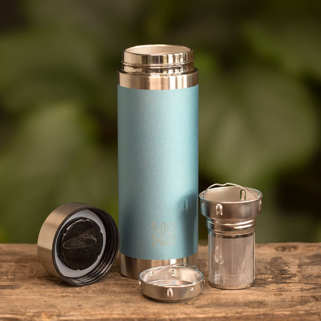 Een geïsoleerde Yoko Design drinkfles Blue Glitter 350 ml met losse deksel, metalen filter en binnenwerk op een houten ondergrond.