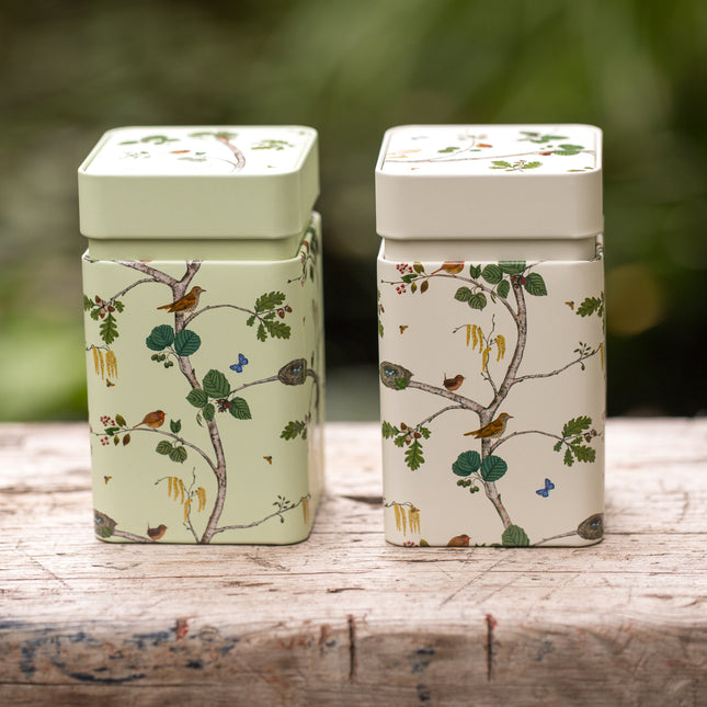 Twee vierkante theeblikken van 150 gram, één lichtgroen en één crèmekleurig, met afbeeldingen van vogels, takjes en bladeren en bijpassende deksels.