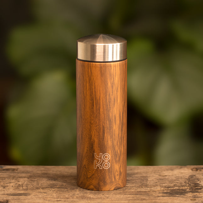 Een geïsoleerde Yoko Design theepot van 350 ml met houtpatroon en metalen deksel staat op hout, met bladeren op de achtergrond.