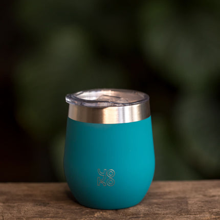 Een geïsoleerde theemok met deksel in blauw van 250 ml staat op hout, met op het mok Yoko Design en vage groene achtergrond.