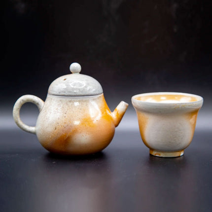 Kleine porseleinen theepot met ronde greep en deksel en bijpassende theekop, wit, grijs en oranje-bruin geglazuurd op donkere basis.