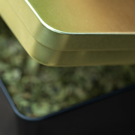Vierkant zwart-gouden blik (9x9x9 cm) met een matgouden deksel van De Theeplantage, gedeeltelijk gevuld met losse groene thee.